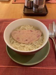 A piece of cured meat sits atop a bed of noodles and soup.